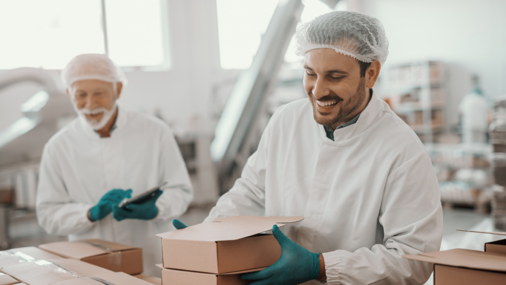 Employees wearing protective clothing in a food production facility use a tablet for digital process control.